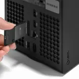 Dłoń wkłada kartę pamięci 2TB do dedykowanego portu rozszerzeń konsoli Xbox Series X, obok innych portów.