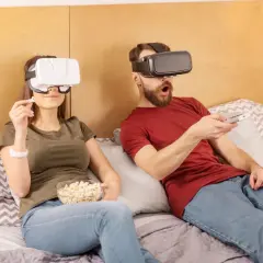 Para jak oglądać filmy VR na komputerze: para w goglach VR leży w łóżku, jedząc popcorn i trzymając pilota.