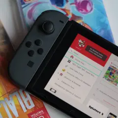 Nintendo Switch z grami, w tym Splatoon 3. Na ekranie widoczne menu z opcjami, jak "Online Play" i "Save Data Cloud", sugerujące datę premiery i funkcje konsoli.