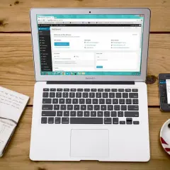 Laptop z panelem WordPress, notatnik z długopisem, telefon i filiżanka kawy. Idealne miejsce do nauki, jak zainstalować WordPress na komputerze.