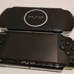 Dwa czarne modele przenośnej konsoli Sony PSP, jeden na drugim. Górny model z logo PSP i napisem UMD. Dolny model z ekranem, przyciskami i analogiem. Nowe psp gotowe do gry.