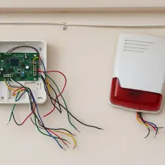 Otwarta centrala alarmowa z kolorowymi przewodami i syrena. Jaki kabel do alarmu w domu? To zależy od systemu.