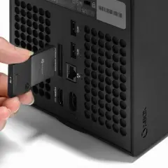 Dłoń wkłada kartę pamięci 2TB do dedykowanego portu rozszerzeń konsoli Xbox Series X, obok innych portów.