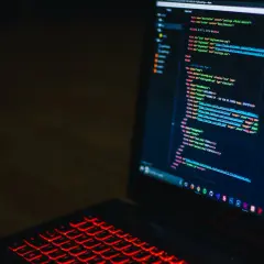 Kod HTML na ekranie laptopa z podświetlaną na czerwono klawiaturą. Widać fragmenty kodu, które mogą pomóc w nauce, jak zmienić kolor tła html.