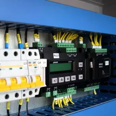 Panel sterowania z modułami PLC, wyłącznikami i przewodami. Pokazuje, jak zastosować system binarny w praktyce do sterowania maszynami.