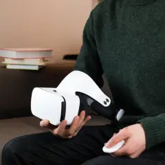 Osoba w zielonym swetrze trzyma białe okulary VR i kontroler. Dowiedz się, jak podłączyć okulary VR do komputera.