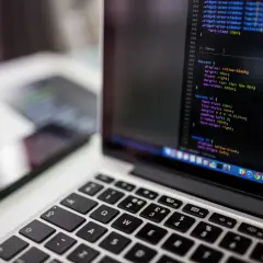 Kod CSS na ekranie laptopa pokazuje, jak wyśrodkować tekst w HTML. Obok leży smartfon.