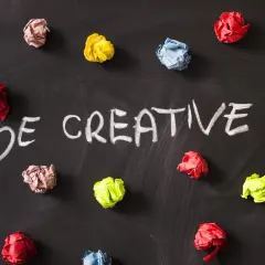 Kolorowe kulki papieru na czarnej tablicy, z napisem "BE CREATIVE!". To inspiracja, jak oszukać system binarny, myśląc nieszablonowo.
