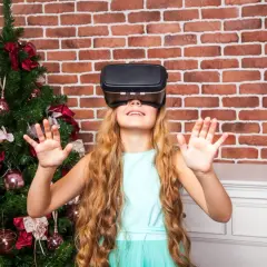 Dziewczynka w okularach VR obok choinki. Czy okulary VR są szkodliwe dla dzieci? To pytanie nurtuje wielu rodziców.
