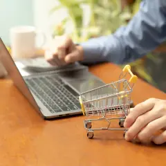 Osoba przy laptopie z małym wózkiem sklepowym uczy się, jak założyć sklep na WordPress.