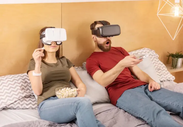 Para jak oglądać filmy VR na komputerze: para w goglach VR leży w łóżku, jedząc popcorn i trzymając pilota.