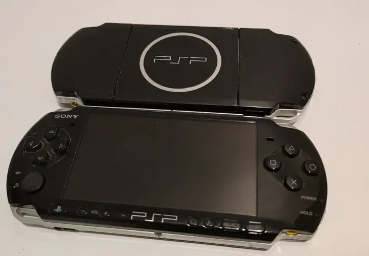 Dwa czarne modele przenośnej konsoli Sony PSP, jeden na drugim. Górny model z logo PSP i napisem UMD. Dolny model z ekranem, przyciskami i analogiem. Nowe psp gotowe do gry.
