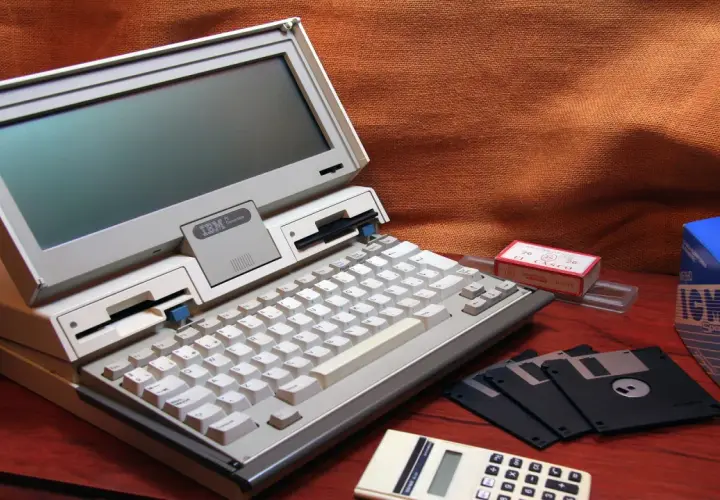 Stary komputer IBM PC Convertible, dyskietki i kalkulator. Kto wymyślił system binarny? To pytanie zadajemy, patrząc na te relikty przeszłości.