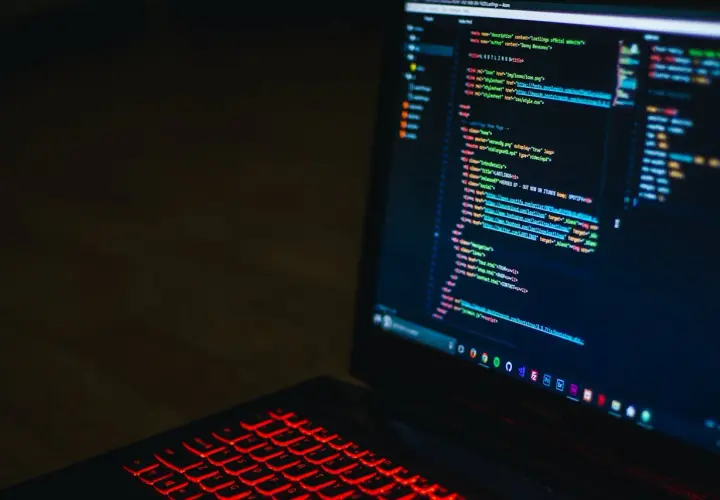 Kod HTML na ekranie laptopa z podświetlaną na czerwono klawiaturą. Widać fragmenty kodu, które mogą pomóc w nauce, jak zmienić kolor tła html.