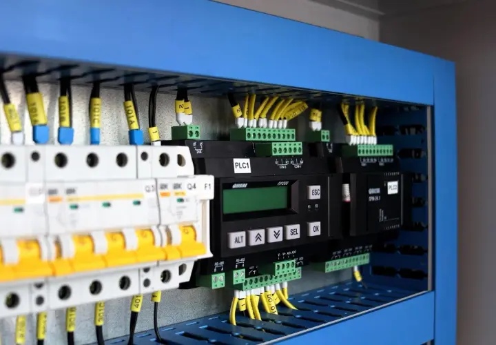 Panel sterowania z modułami PLC, wyłącznikami i przewodami. Pokazuje, jak zastosować system binarny w praktyce do sterowania maszynami.