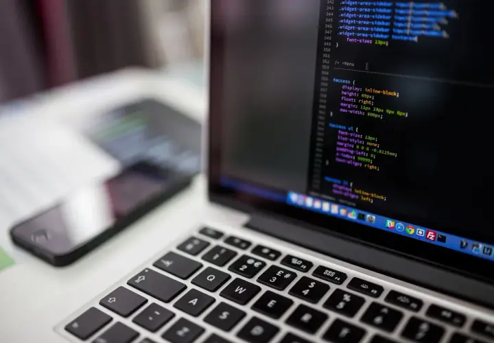 Kod CSS na ekranie laptopa pokazuje, jak wyśrodkować tekst w HTML. Obok leży smartfon.