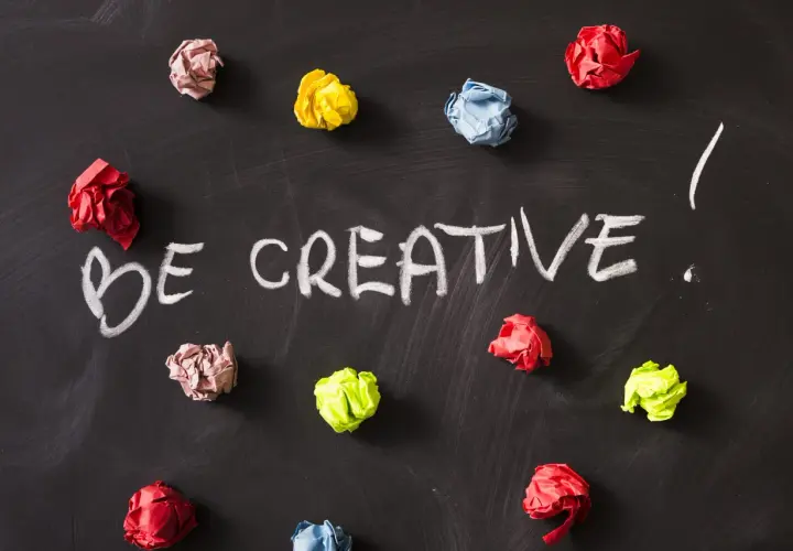 Kolorowe kulki papieru na czarnej tablicy, z napisem "BE CREATIVE!". To inspiracja, jak oszukać system binarny, myśląc nieszablonowo.