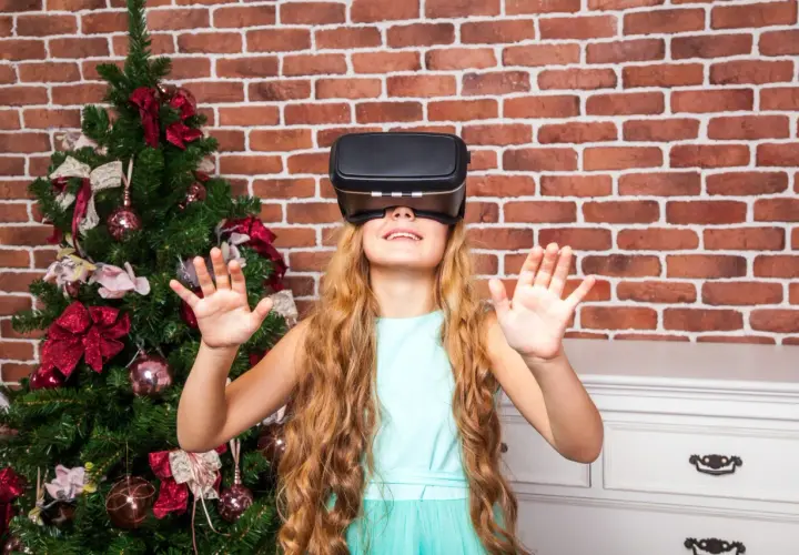 Dziewczynka w okularach VR obok choinki. Czy okulary VR są szkodliwe dla dzieci? To pytanie nurtuje wielu rodziców.