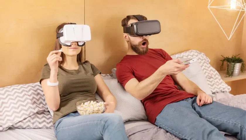 Para jak oglądać filmy VR na komputerze: para w goglach VR leży w łóżku, jedząc popcorn i trzymając pilota.