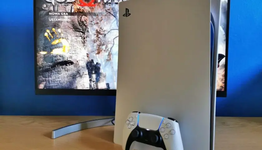 Konsola PlayStation 5 z kontrolerem DualSense obok. Na ekranie widoczny tytuł gry "God of War" i opcje "Nowa gra", "Ustawienia". Idealny moment na playstation aktualizacja.