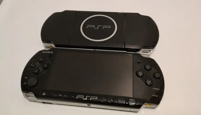 Dwa czarne modele przenośnej konsoli Sony PSP, jeden na drugim. Górny model z logo PSP i napisem UMD. Dolny model z ekranem, przyciskami i analogiem. Nowe psp gotowe do gry.