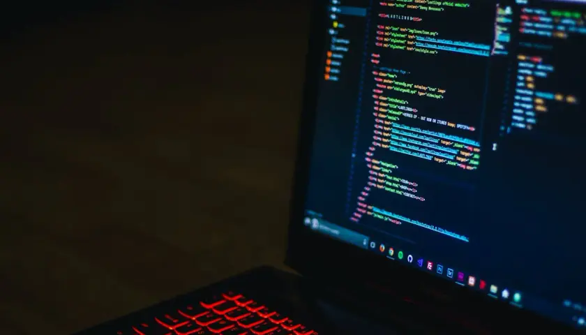 Kod HTML na ekranie laptopa z podświetlaną na czerwono klawiaturą. Widać fragmenty kodu, które mogą pomóc w nauce, jak zmienić kolor tła html.