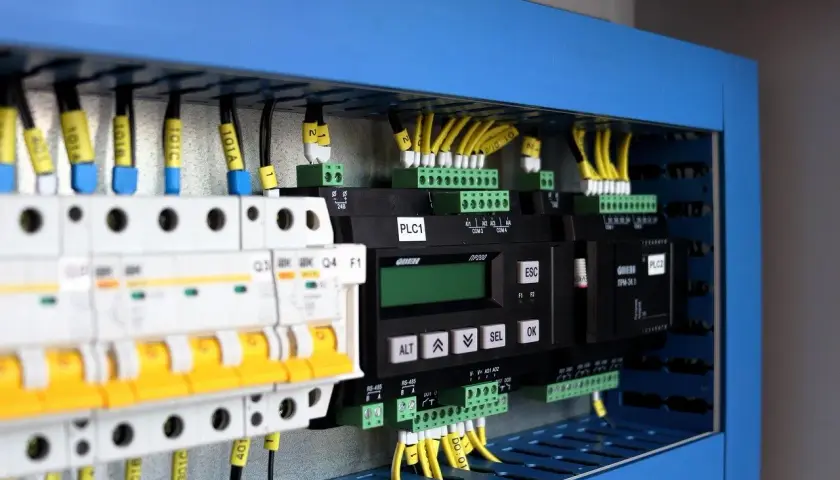 Panel sterowania z modułami PLC, wyłącznikami i przewodami. Pokazuje, jak zastosować system binarny w praktyce do sterowania maszynami.