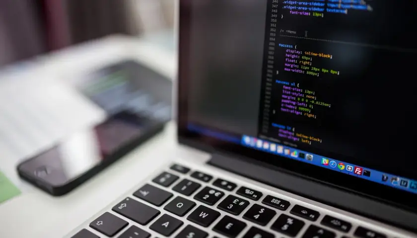Kod CSS na ekranie laptopa pokazuje, jak wyśrodkować tekst w HTML. Obok leży smartfon.