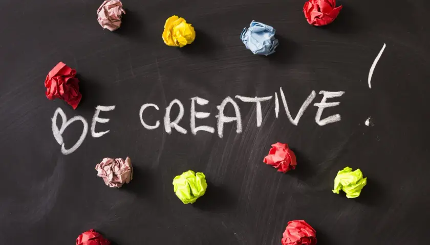 Kolorowe kulki papieru na czarnej tablicy, z napisem "BE CREATIVE!". To inspiracja, jak oszukać system binarny, myśląc nieszablonowo.