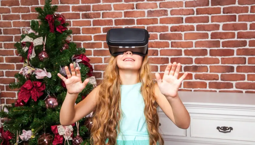 Dziewczynka w okularach VR obok choinki. Czy okulary VR są szkodliwe dla dzieci? To pytanie nurtuje wielu rodziców.