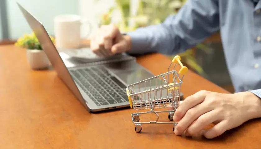 Osoba przy laptopie z małym wózkiem sklepowym uczy się, jak założyć sklep na WordPress.