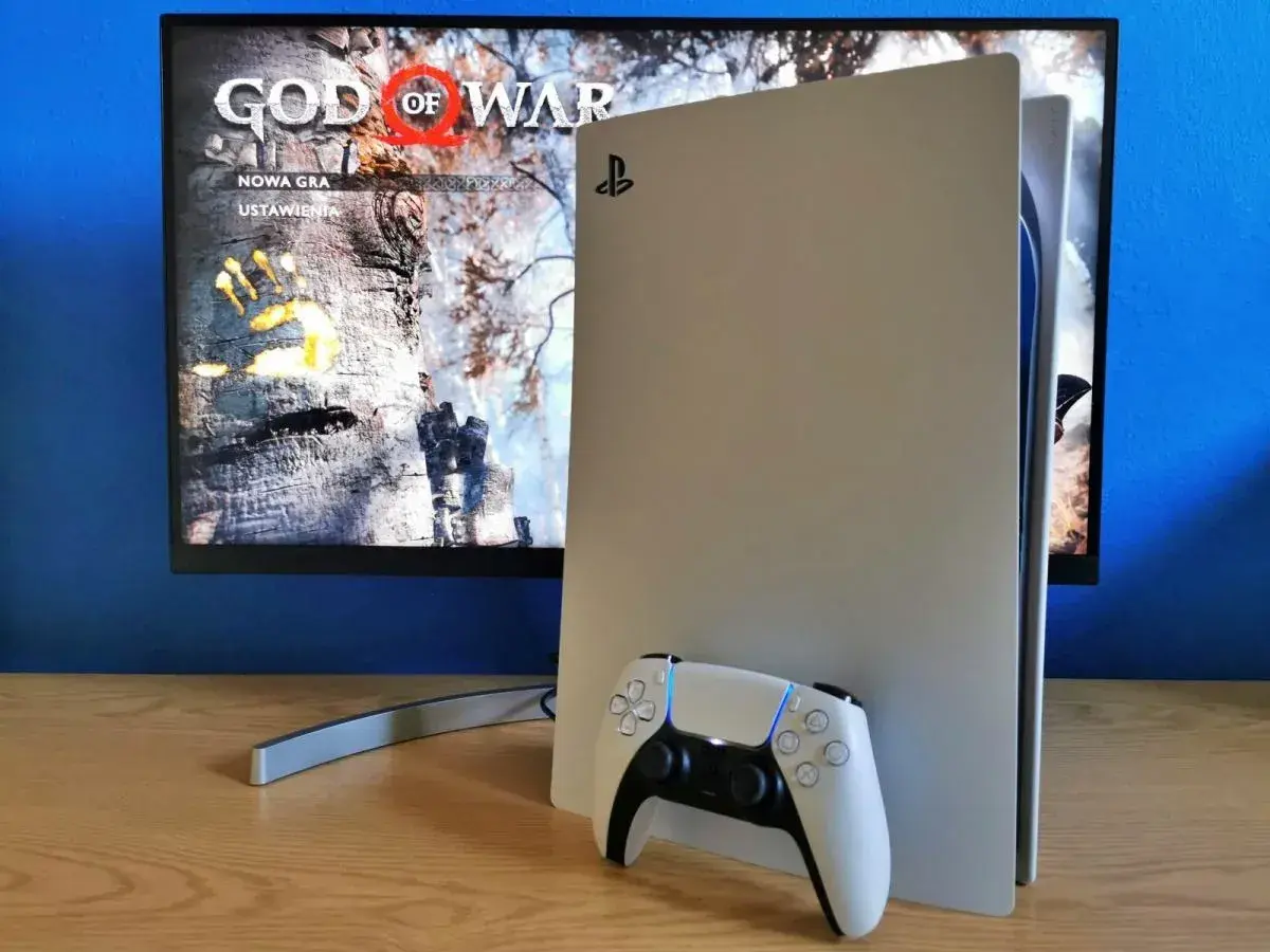 Konsola PlayStation 5 z kontrolerem DualSense obok. Na ekranie widoczny tytuł gry "God of War" i opcje "Nowa gra", "Ustawienia". Idealny moment na playstation aktualizacja.
