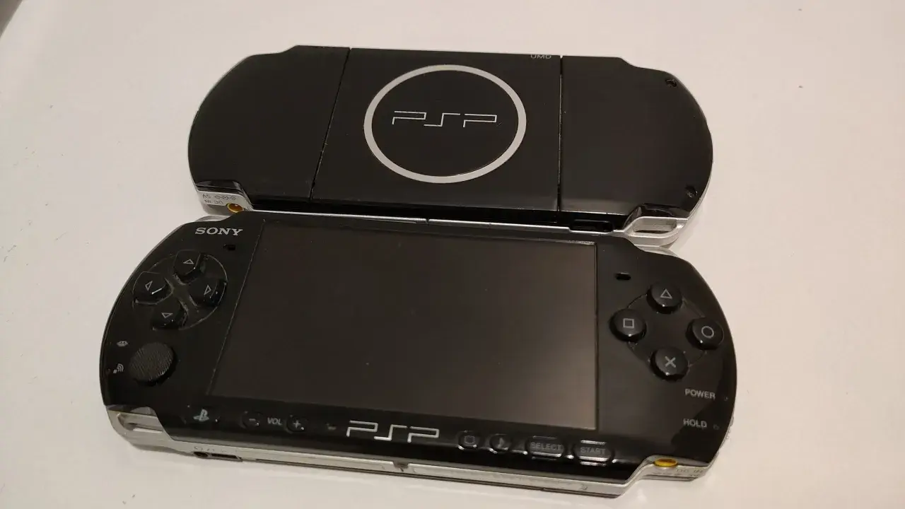 Dwa czarne modele przenośnej konsoli Sony PSP, jeden na drugim. Górny model z logo PSP i napisem UMD. Dolny model z ekranem, przyciskami i analogiem. Nowe psp gotowe do gry.