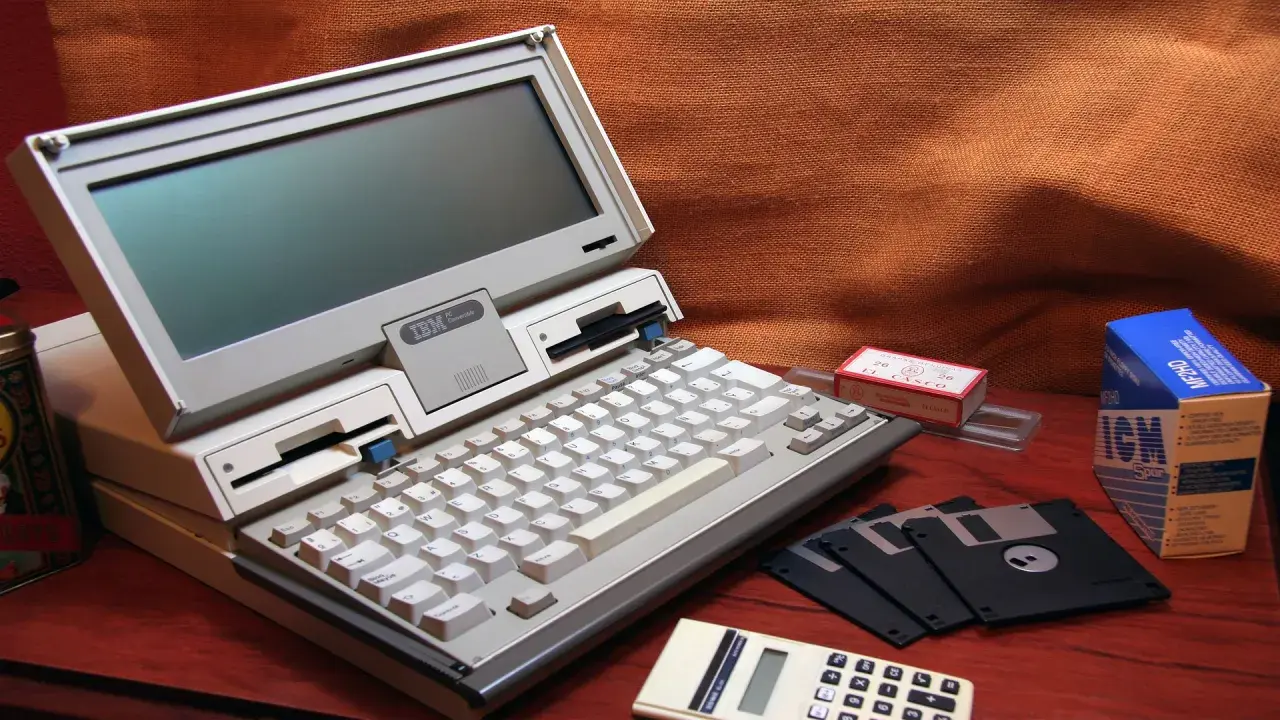 Stary komputer IBM PC Convertible, dyskietki i kalkulator. Kto wymyślił system binarny? To pytanie zadajemy, patrząc na te relikty przeszłości.