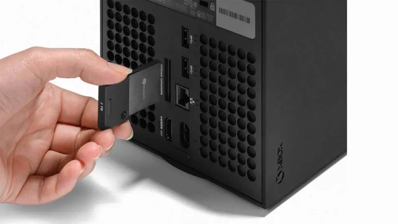 Dłoń wkłada kartę pamięci 2TB do dedykowanego portu rozszerzeń konsoli Xbox Series X, obok innych portów.