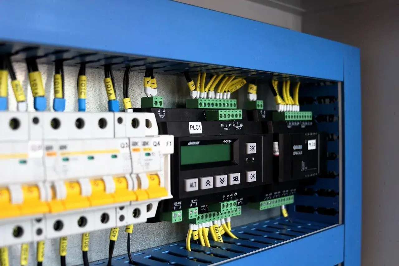 Panel sterowania z modułami PLC, wyłącznikami i przewodami. Pokazuje, jak zastosować system binarny w praktyce do sterowania maszynami.