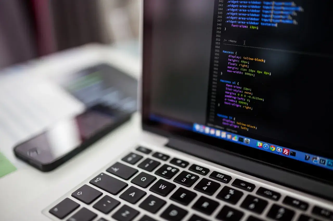 Kod CSS na ekranie laptopa pokazuje, jak wyśrodkować tekst w HTML. Obok leży smartfon.