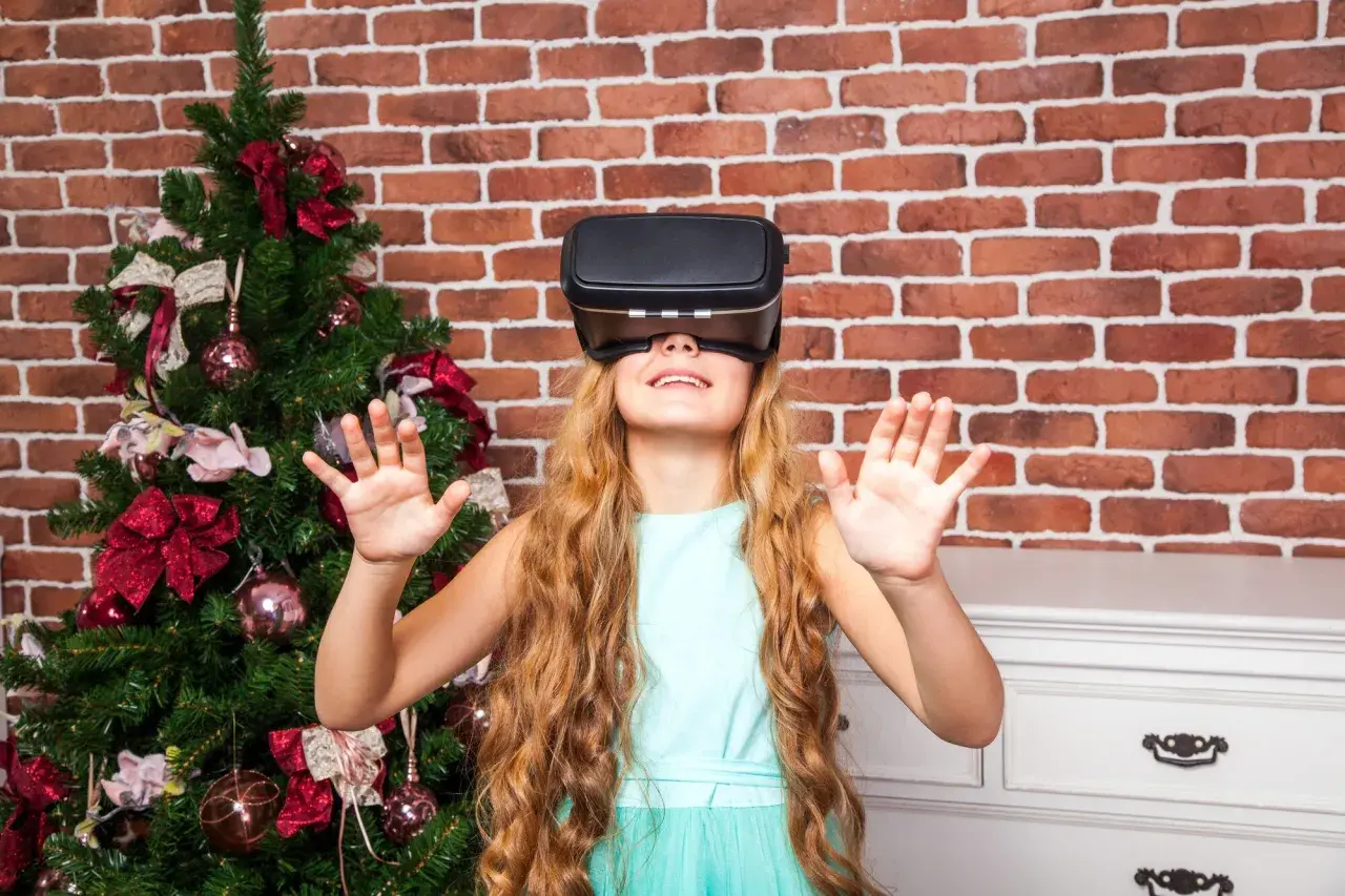 Dziewczynka w okularach VR obok choinki. Czy okulary VR są szkodliwe dla dzieci? To pytanie nurtuje wielu rodziców.