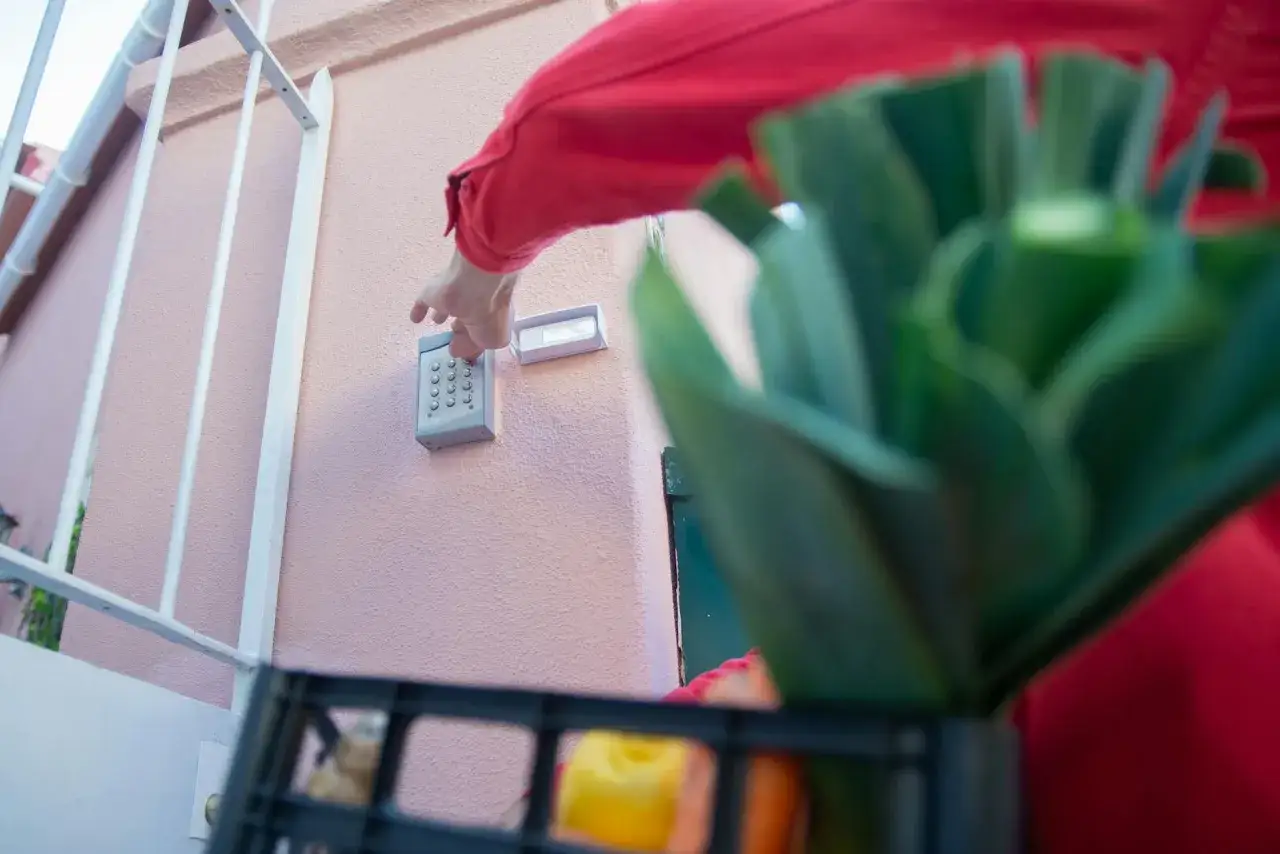 Osoba w czerwonej bluzie naciska przyciski na domofonie, próbując wyłączyć alarm w domu.