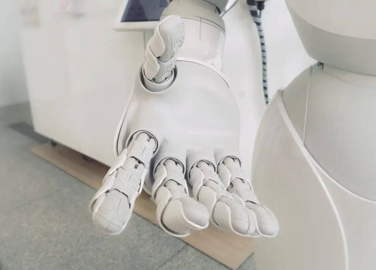 Biała, mechaniczna dłoń robota wyciągnięta w geście powitania. Czy sztuczna inteligencja zastąpi człowieka?