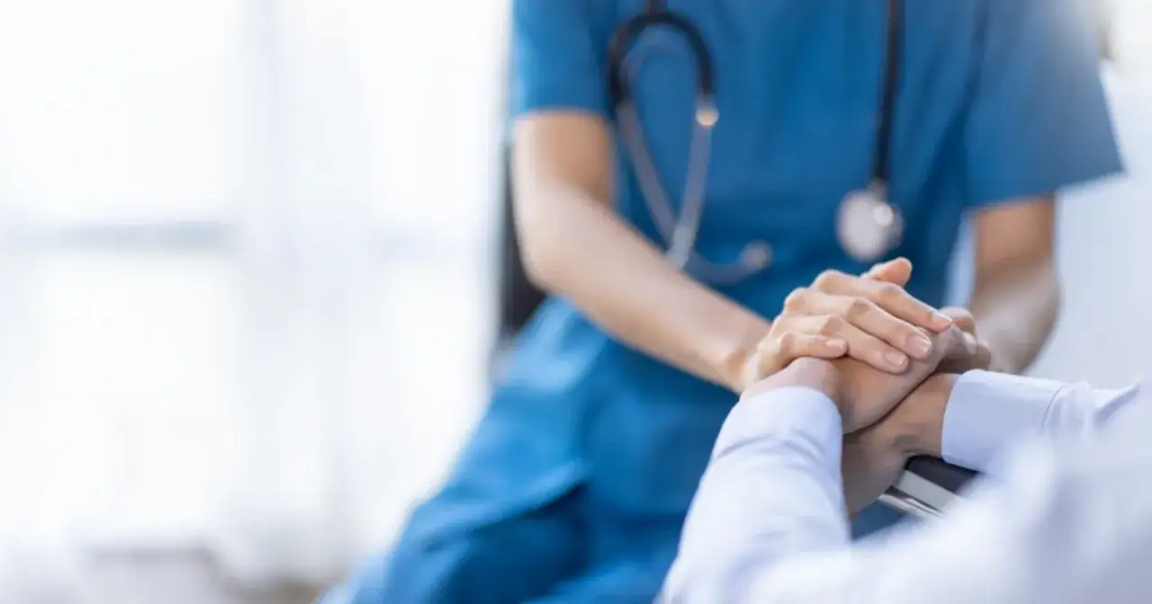 Dłoń pielęgniarki w niebieskim fartuchu wspiera dłoń pacjenta. Czy sztuczna inteligencja zastąpi lekarzy? Empatia i dotyk pozostają kluczowe.