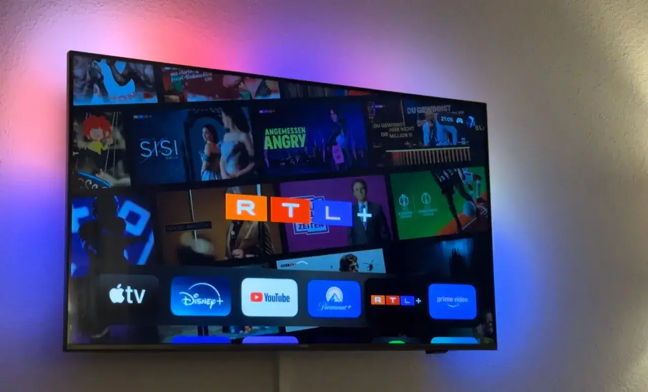 Telewizor z kolorowym podświetleniem, na ekranie aplikacje Apple TV, Disney+, YouTube, Prime Video i RTL+.